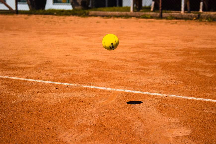 Piłka tenisowa spadająca w okolice linii końcowej kortu ziemnego