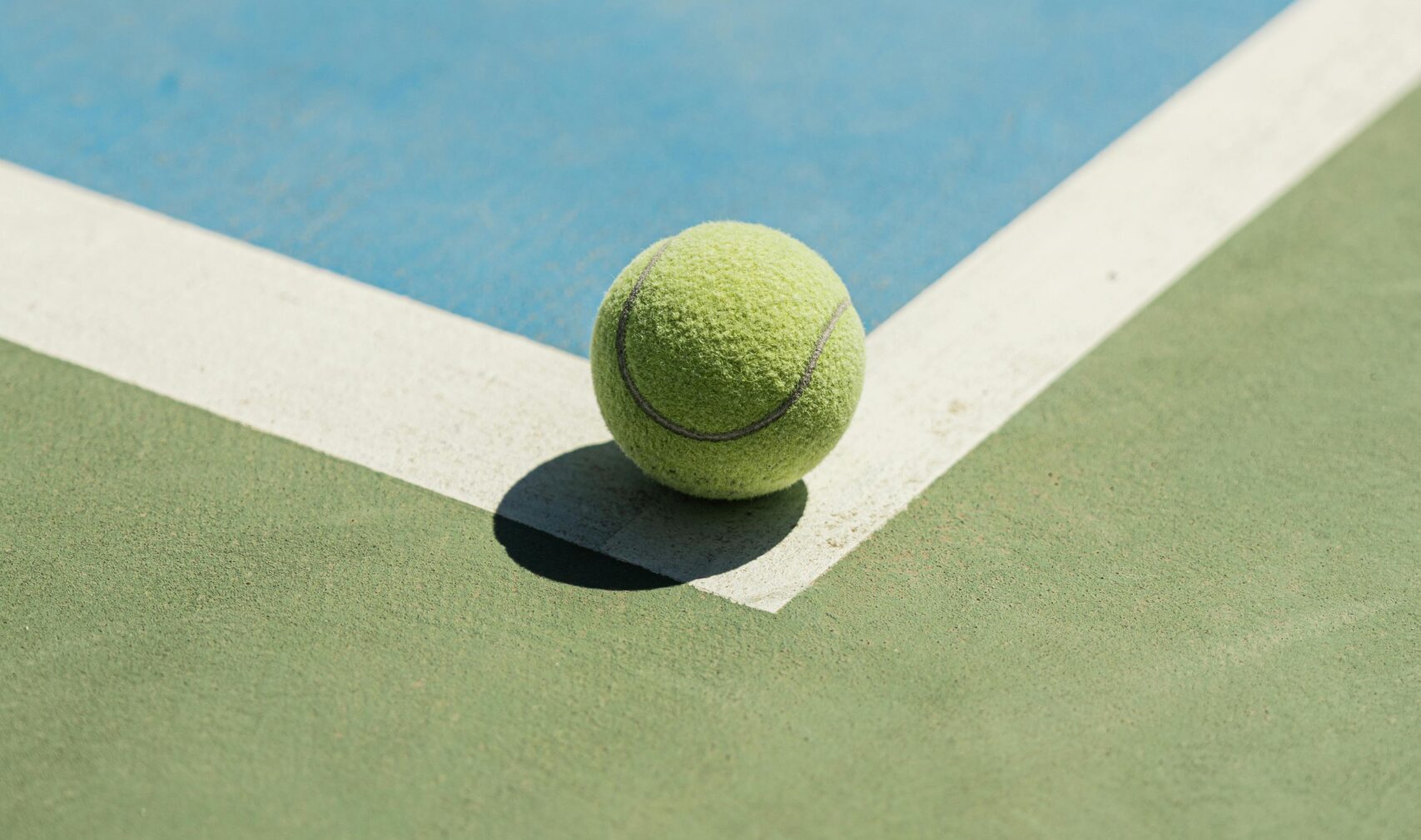 Zbliżenie na piłkę tenisową, leżącą na samym narożniku kortu
