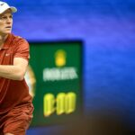 Jannik Sinner przymierza się do forehandu na tle zegara