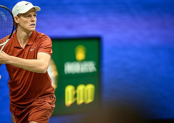 Jannik Sinner przymierza się do forehandu na tle zegara