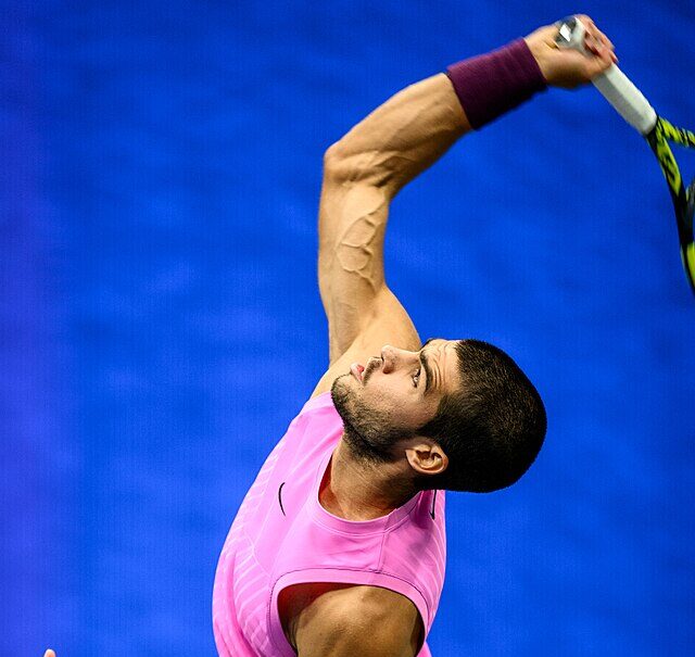 Carlos Alcaraz patrzy w kierunku wyrzuconej piłki podczas serwisu