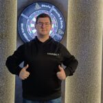 Sebastian Białecki stojący na tle tarczy z kciukami w górę