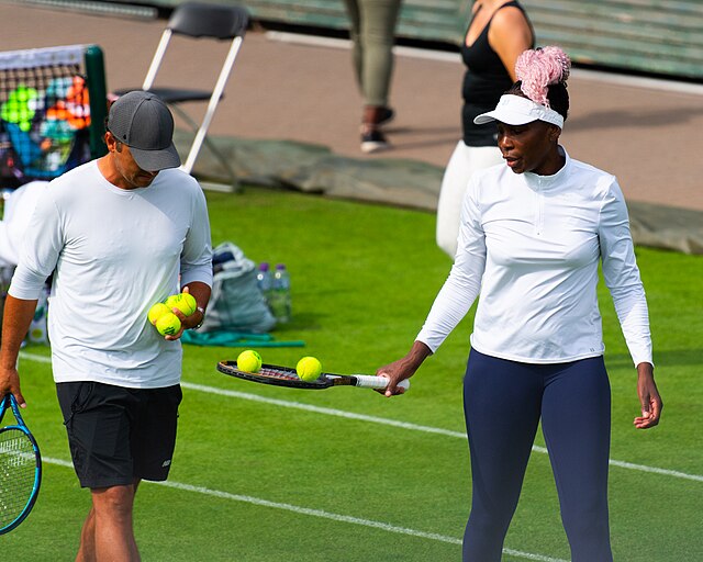 Venus Williams z wystawioną rakietą odbiera piłki tenisowe od trenera podczas treningu