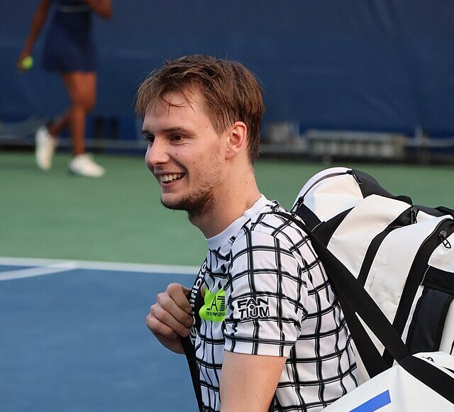 Uśmiechnięty Alexander Bublik opuszcza kort z torbami na barkach