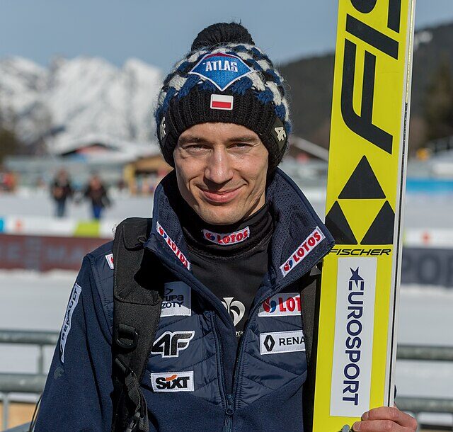 Uśmiechnięty Kamil Stoch z nartami w ręce