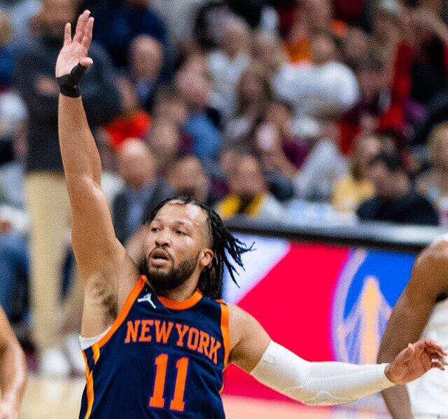 Jalen Brunson z wystawioną rękę w górze próbuje powstrzymać obrońców