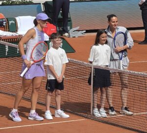Iga Świątek i Marta Kostyuk ustawione przy siatce z dziećmi